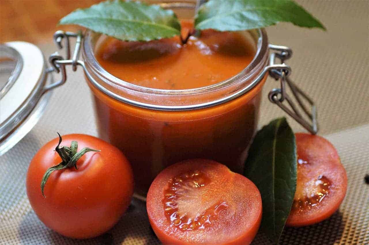 Tomato soup served in a canning jar, surrounded by fresh tomato fruits.